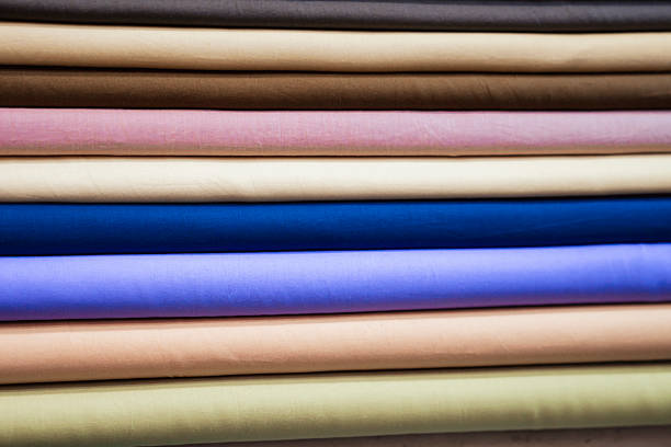 A close-up shot reveals a meticulously arranged stack of fabric rolls, showcasing a diverse palette of colors and textures.  Each roll displays a unique hue, ranging from soft pastels to rich, deep tones, highlighting the variety and potential of this textile collection. The image's composition emphasizes the smooth surfaces and subtle variations in the fabric's texture, inviting viewers to appreciate the tactile qualities of the materials.