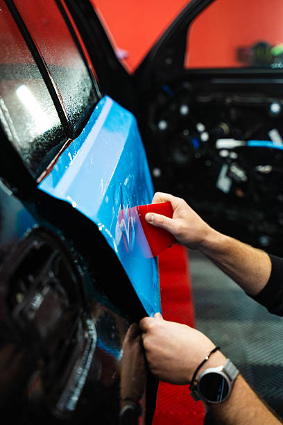 istock Vehicle wrap detailing involves squeegee strokes for seamless, wrinkle-free adhesion. Detailing expert uses red squeegee wrapper to flatten blue PPF wrap on car surface. 2220466715