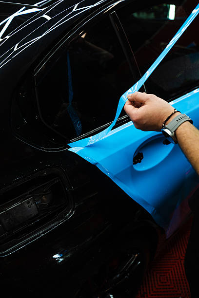 istock Precision cutting of PPF wrap on car body. Precision PPF wrapping and detailing on car panel using sharp blade to trim wrap with accuracy. Car detailing involves precise vinyl cutting techniques. 2220466767