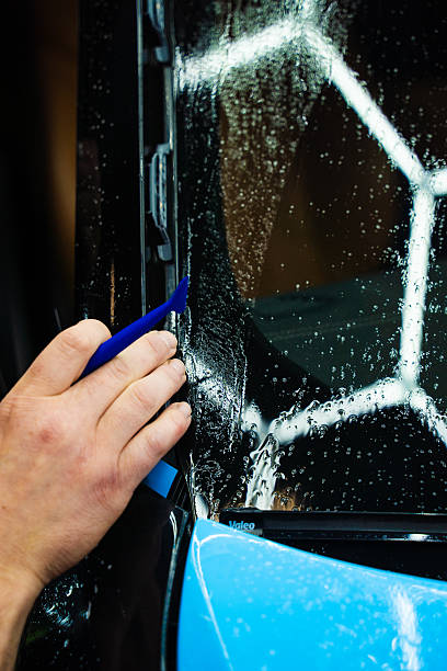 istock Micro squeegee to press blue vinyl wrap deep into tight vehicle trim gaps. Micro squeegee tool ensures seamless adhesion during car wrap installation. Micro Squeegee on Trim Wrap. 2220467017