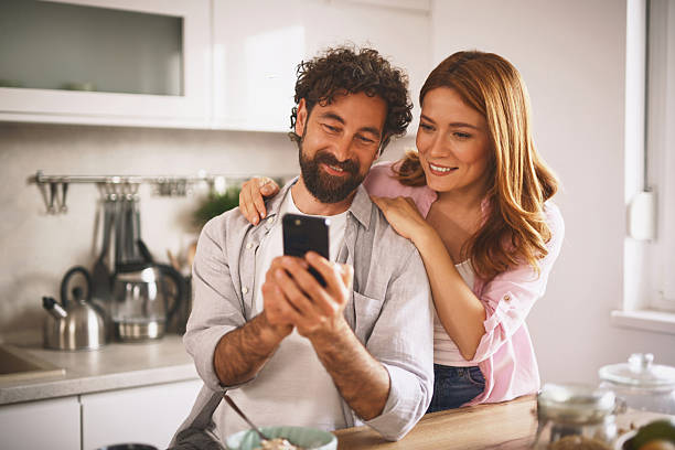 istock Happy couple using smartphone and having breakfast in kitchen 2220467193