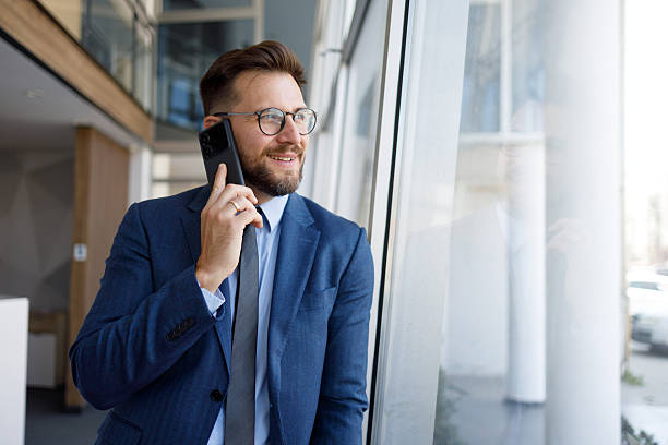istock Professional executive speaking on mobile, standing near glass window inside contemporary corporate workspace 2220467559