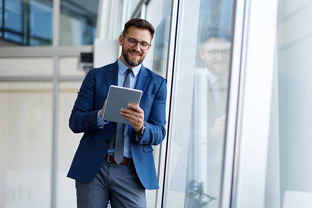 istock Professional businessman working on digital tablet, standing in contemporary office interior, embodying corporate success and innovation 2220467903