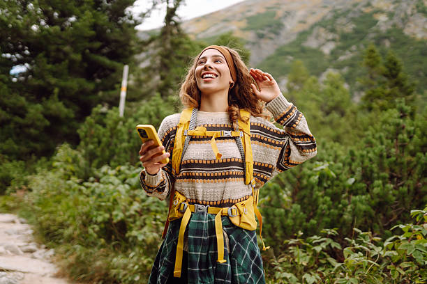 istock Smiling female hiker with bright yellow backpack using phone on hiking trail. 2220468169