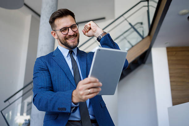 Excited businessman celebrating success while looking at a digital tablet in a modern office, radiating positivity and joy