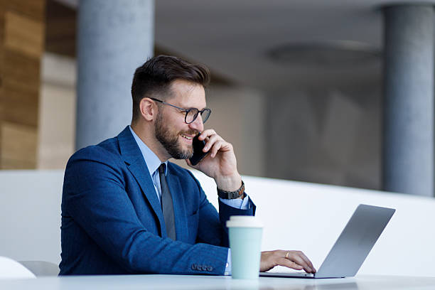 istock Professional businessman multitasking, typing on laptop and talking on smartphone in contemporary workplace setting 2220469549