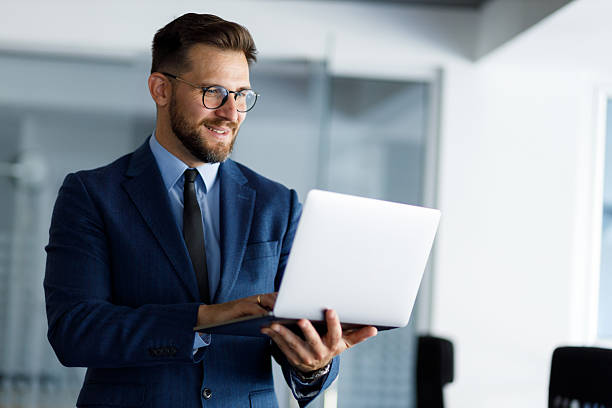 istock Professional businessman working on laptop, standing in sleek office space, combining tech-savvy expertise with corporate style 2220470137