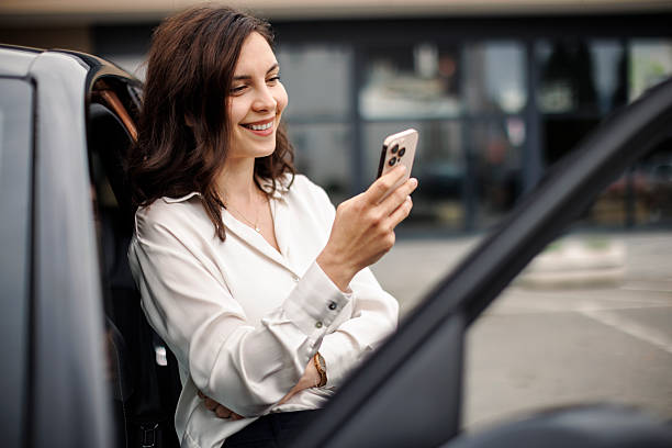 istock Smiling businesswoman using smart phone by her parked car 2220471702