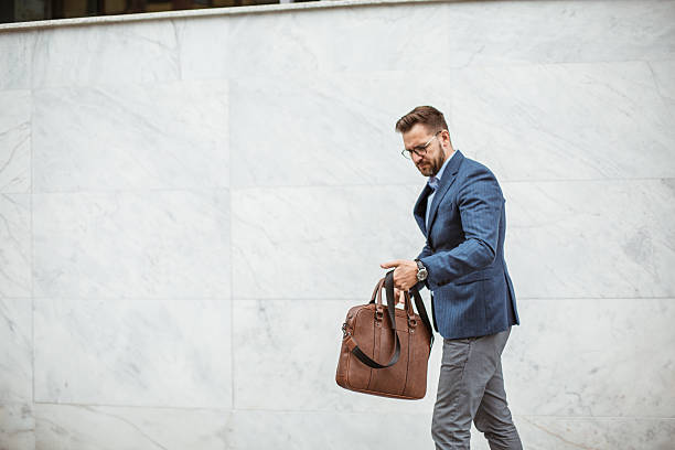 istock Businessman walking near marble wall holding briefcase 2220476772