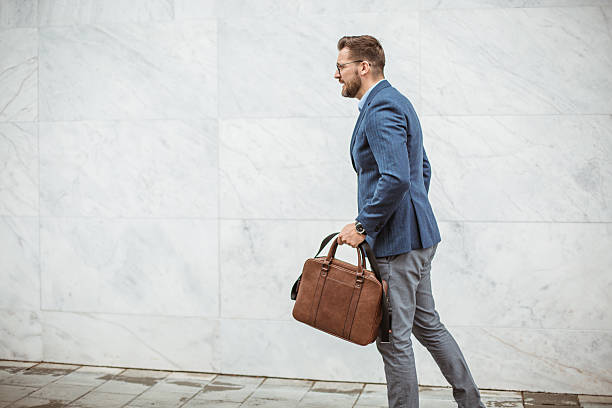 istock Businessman walking briskly along marble wall carrying briefcase 2220476776