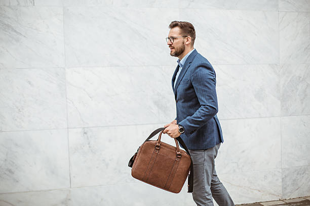 istock Businessman walking briskly along marble wall carrying briefcase 2220476796