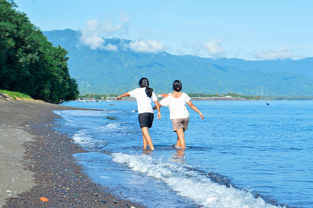 istock Two girls walking happily along sunny coastal surf 2220478601