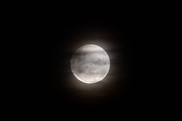 istock A photo of the moon during a partial eclipse, with its top edge slightly darkened and a soft haze from thin clouds diffusing the light 2220483099
