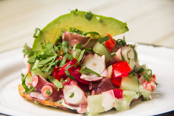 istock This visually appealing dish features a tostada topped with colorful octopus salad, fresh vegetables, and garnished with avocado, highlighting a fusion of flavors and textures. 2220486393
