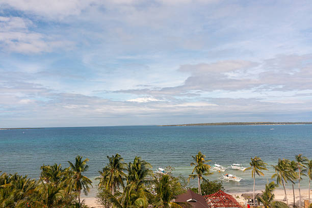 Beach view from above, palm trees and ocean waves crashing on white sands. Baigad Lagoon Beach. Bantayan Island, Cebu, Philippines.