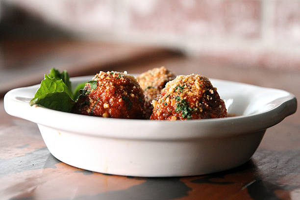 A side angle captures a bowl of meatballs in tomato sauce, topped with herbs and cheese. The setting hints at cozy dining and comforting meals.