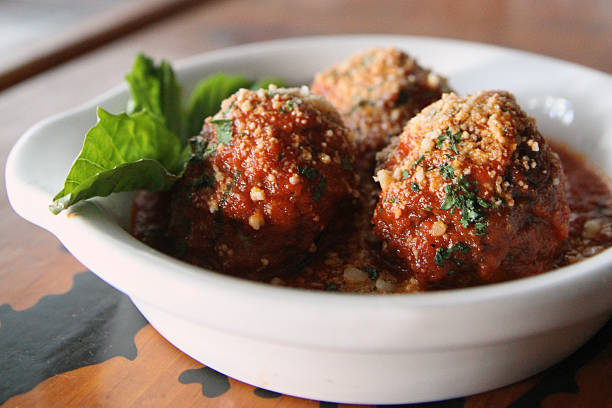 A bowl of Italian-style meatballs rests in tomato sauce, garnished with fresh basil and grated cheese. The dish evokes warmth, comfort, and traditional home cooking.