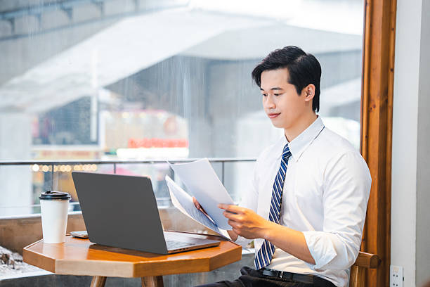 istock Business professional reviews documents at cafe with laptop; remote work in a cozy setting 2220501967