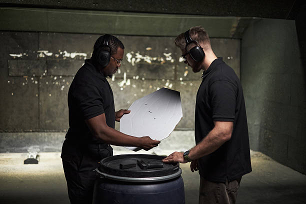 istock Two Young Men Analyzing Paper Target after Shooting Practice Indoors 2220504124