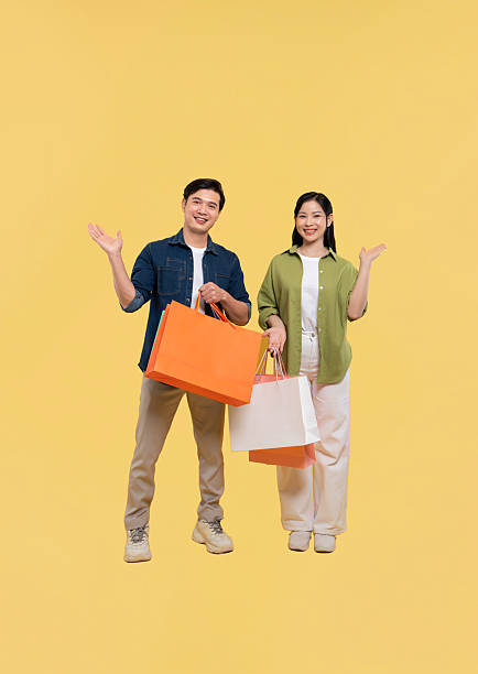 istock Smiling couple stands with shopping bags presenting an inviting gesture on a vibrant backdrop 2220506439