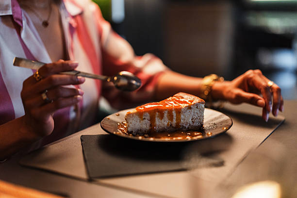 A person appreciates a decadent slice of cheesecake drizzled with caramel in an upscale dining environment. The focus is on indulgence and culinary enjoyment.