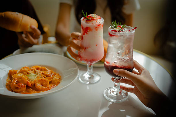 Female hands gently grasping a sparkling cherry soda glass on a wooden dinner table. Bright red bubbles and a festive mood make it perfect for summer, celebration, or casual lifestyle themes.