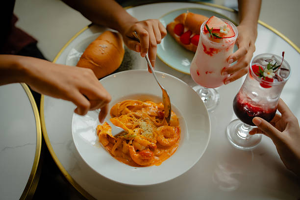 Top view of Woman's hand holding a chilled cherry soda drink with ice and bubbles on a dining table. Bright red beverage contrasts with the clean table setting, ideal for food, drink, and lifestyle concepts.