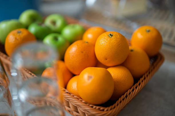 Close-up of a wicker basket filled with fresh oranges and green apples on a kitchen counter in natural light.