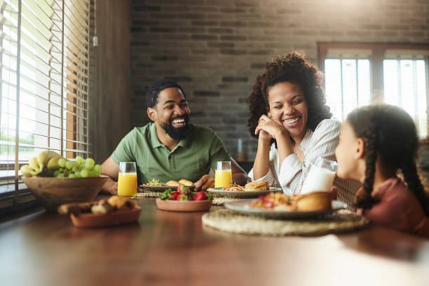 Happy African American parents communicating with their daughter while having a meal in dining room. Copy space.