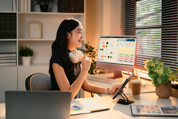 istock Female graphic designer using digital tablet in a modern workspace filled with color charts and design tools 2220519397