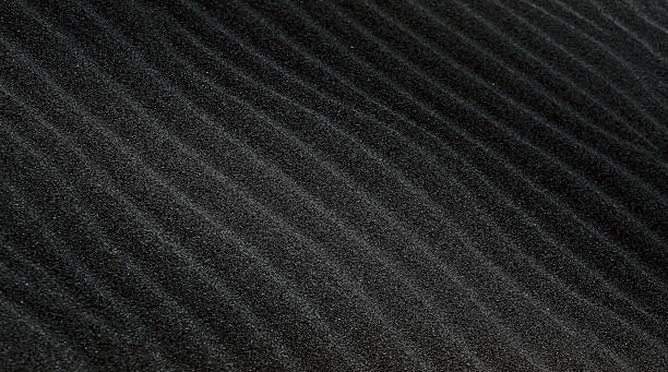 istock An abstract dark background with wavy black sand closeup. 2220520940