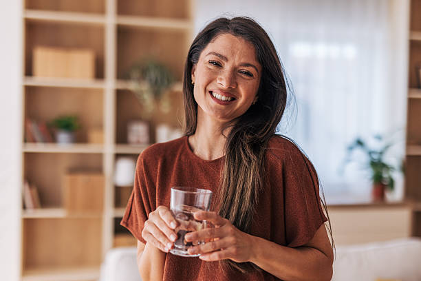 istock Happy young woman drinking water at home and smiling at camera 2220526708