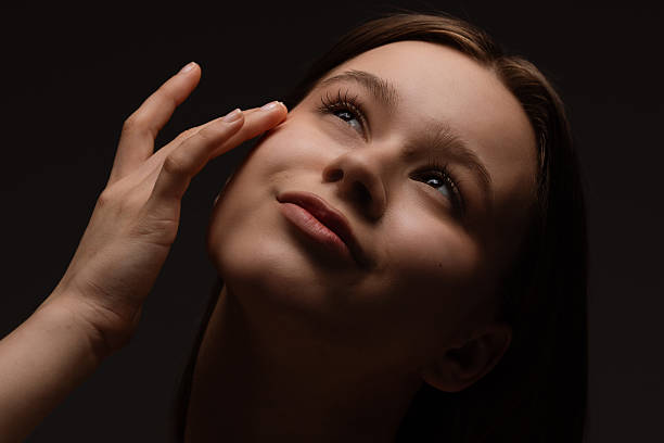 istock Young Woman Admiringly Touching Her Face Under Soft Lighting 2220527699