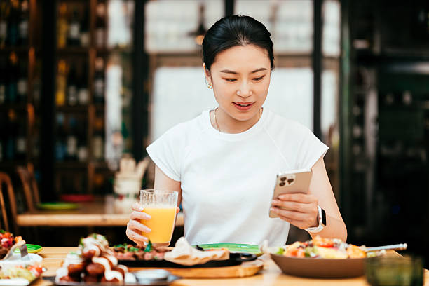istock Smiling young Asian woman using smartphone while enjoying her lunch in restaurant. Luxury lifestyle.  Enjoying life with good food. People, food, lifestyle and technology. 2220529641