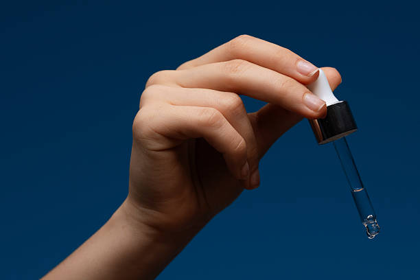 istock Hand Holding Cosmetic Dropper with Liquid on Blue Background 2220529905