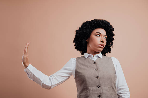 istock Confident young professional woman making a hand gesture against a beige backdrop, showcasing elegance and style 2220531883