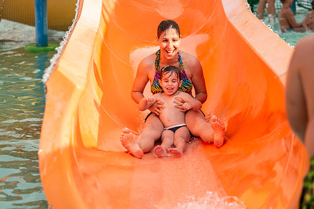 Mother and daughter enjoying a fun-filled day, sliding down an orange waterslide at a water park, creating a cherished summer memory