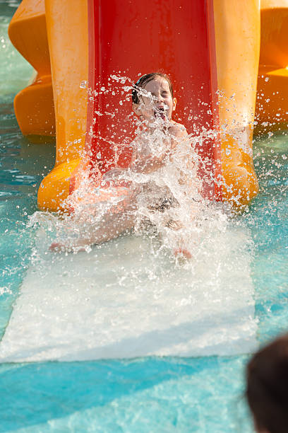 Happy summer scene of two boys sliding trough a yellow wet plastic in the garden