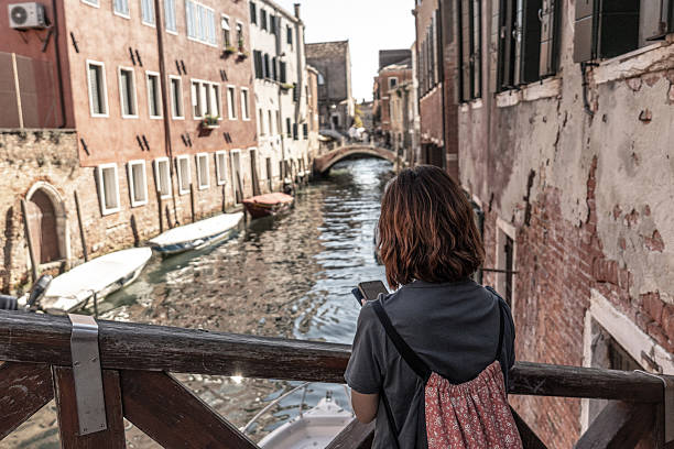 istock Young tourist using smartphone and admiring venice canal view from bridge 2220534107
