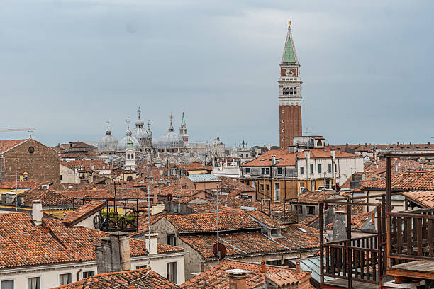 Red tiled roofs and the bell tower of st. Mark's square create a picturesque view of venice, italy, under a cloudy sky