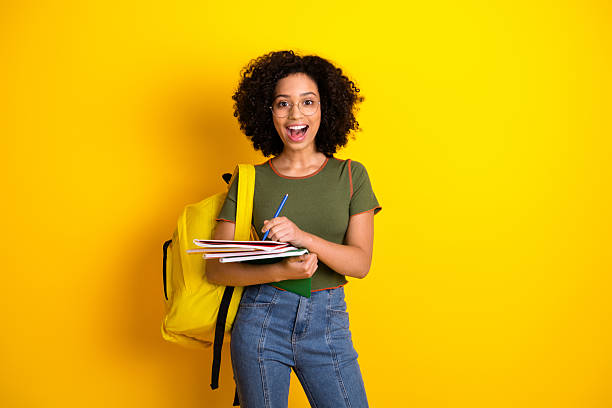 istock Cheerful student holding notebooks and writing, wearing casual clothes with a bright yellow background, expressing happiness 2220534492