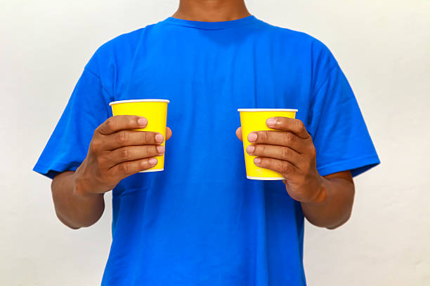 A man in a blue shirt holds two yellow cups, studio shot against a white background.