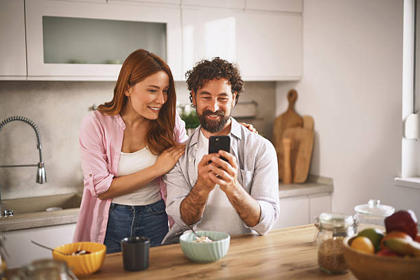 istock Happy couple using smartphone and having breakfast in the kitchen 2220537422