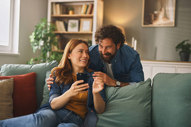 istock Happy couple relaxing on sofa, browsing smartphone together at home 2220537775