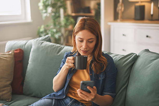 istock Young woman relaxing on sofa, drinking coffee and using smartphone at home 2220538037