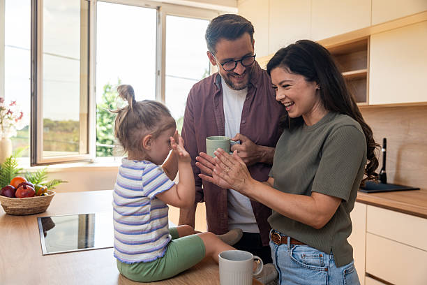 istock Happy parents enjoying peaceful morning together in the kitchen while drinking coffee as their playful young daughter sits on counter smiling and playing with toys. Calm, cozy family moment together. 2220540022