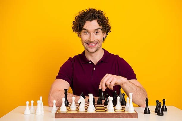 istock Man with a confident smile placing a chess piece on a board against a vibrant yellow background representing strategy 2220540512
