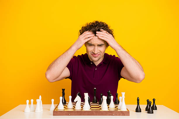 istock Young man focuses intently while playing chess against a vibrant yellow background wearing a burgundy polo shirt 2220540513