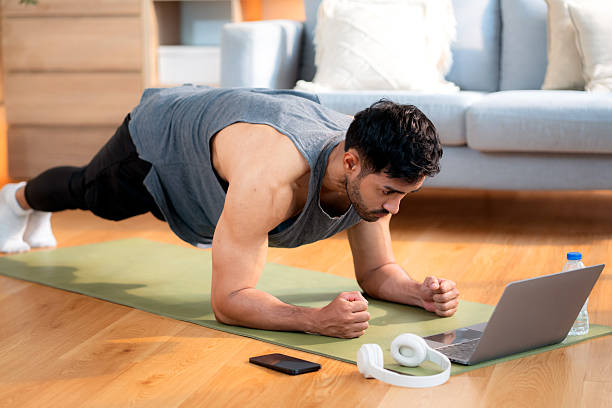 istock Young asian man doing plank exercise in living room at home while watching online workout tutorial on laptop with endurance and motivation, man training plank on yoga mat, digital fitness lifestyle. 2220546390