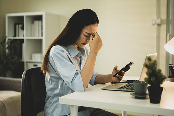 istock Businesswoman feeling stressed while working from home, holding smartphone with eyes closed and pinching nose in frustration 2220552561